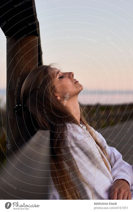 Peaceful woman relaxing on promenade at sundown dreamy traveler sunset carefree calm evening female embankment wooden fence lean nature eyes closed vacation