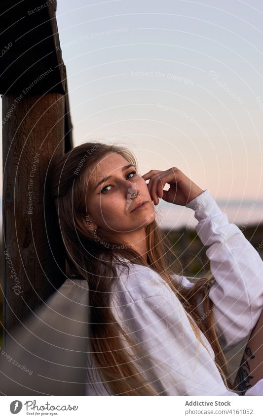 Peaceful woman relaxing on promenade at sundown dreamy traveler sunset carefree calm evening female embankment wooden fence lean nature looking at camera