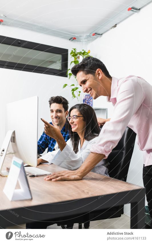 Smiling entrepreneurs discussing project at work in office colleague paper stylish apparel smile computer interact collaborate coworker cooperate teamwork