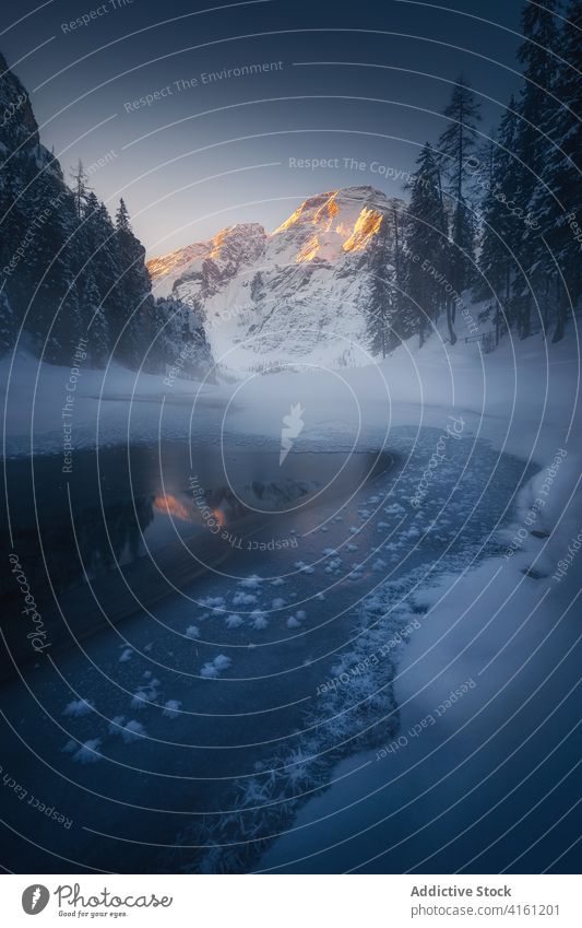 Icy pond reflecting snowy mountain near trees in winter reflection nature highland sky solitude shiny frozen lake grow twilight scenic rough evening ridge