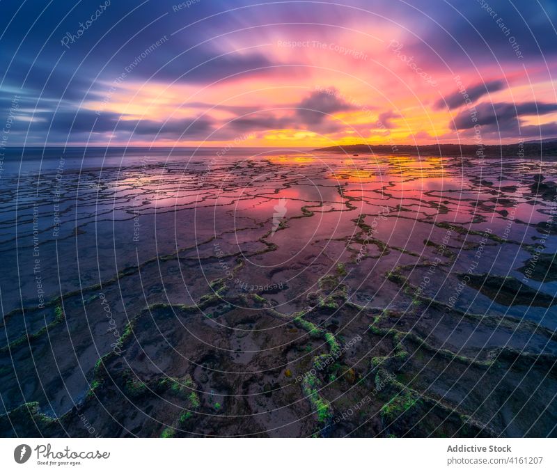 Rough ocean shore under colorful sky at sundown cloudy atmosphere nature seascape horizon untouched crack shabby rough terrain coast bright wavy line water