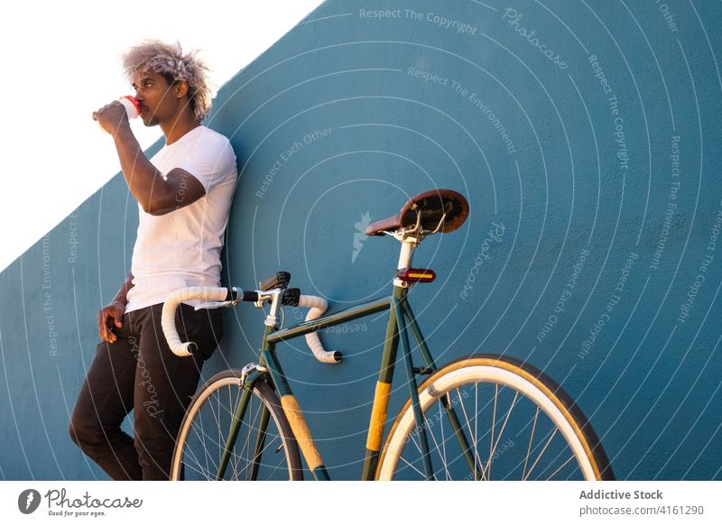 Black man and afro biker drinking takeaway coffee on a blue wall black biker black man black rider black cyclistg drinking coffee coffee latte relax calm