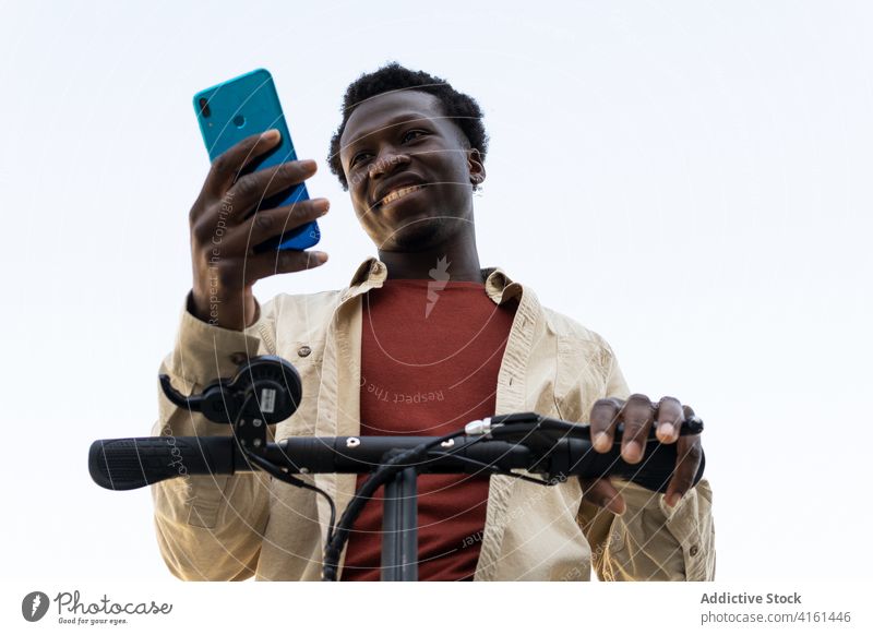 Black man using smartphone and riding scooter browsing city electric street transport gadget male ethnic black african american mobile ride urban internet road