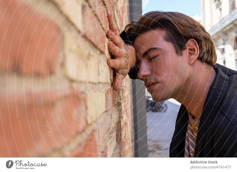 Stylish dreamy tattooed man leaning on rough brick wall eyes closed lean on hand stylish appearance reflective street town trendy shabby natural material urban