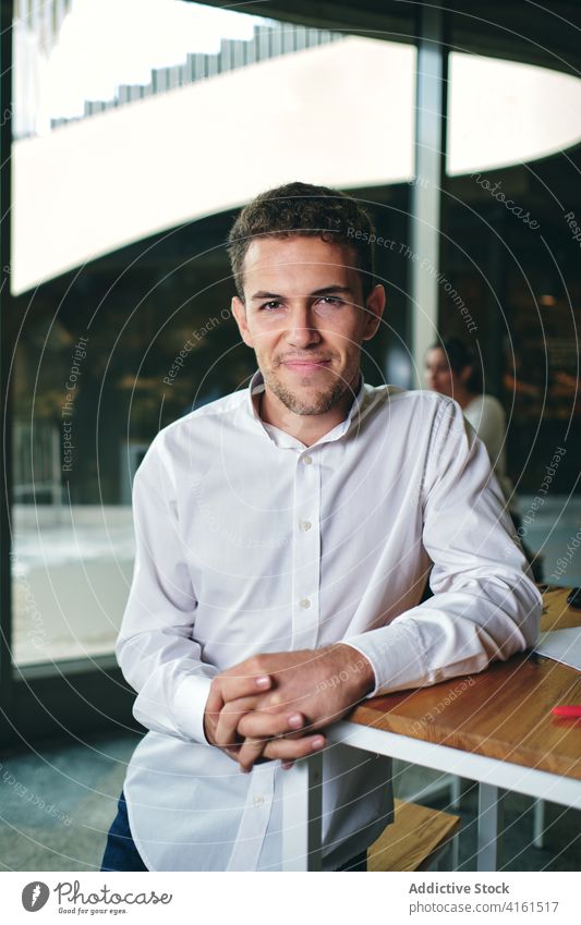 Smiling man in white shirt resting at table glad hands clasped confident satisfied sincere friendly pleasant portrait appearance building smile formal wear