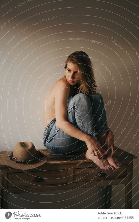 Stylish sensual model on table near wall denim reflective eyes closed topless seductive appearance hairstyle barefoot wear mindfulness woman dreamy feminine