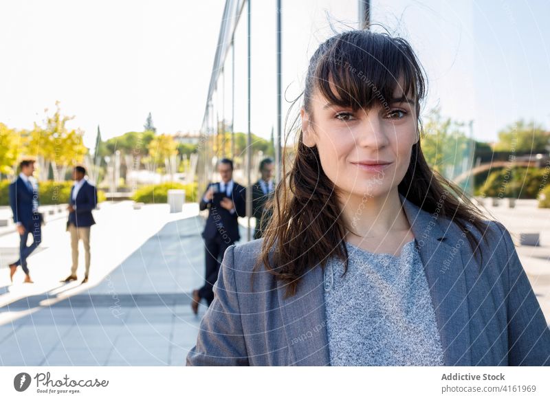 Positive young woman looking at camera on street positive entrepreneur elegant building exterior reflection work happy professional manager job female brunette