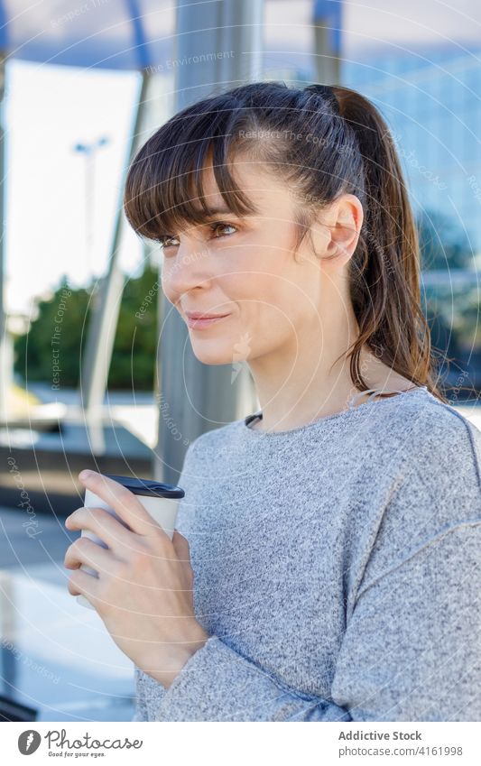 Happy young woman drinking coffee to go near modern building coffee break street positive smile entrepreneur dreamy city urban takeaway cheerful female casual