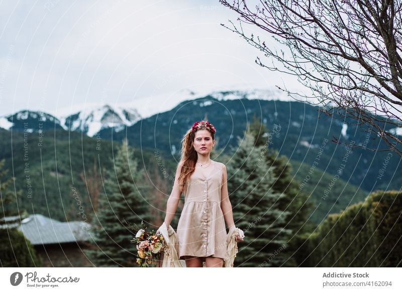 Stylish woman with flowers standing against mountains style boho nature landscape romantic environment bride harmony young female pure fresh freedom trendy