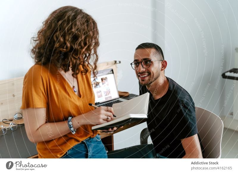 Focused young coworkers discussing project in light office woman take note employee colleague workplace busy job together occupation teamwork casual eyeglasses