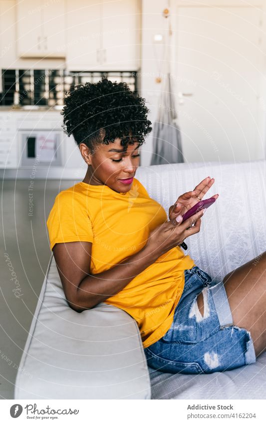 Laughing black woman using smartphone at home laugh having fun excited browsing mobile cheerful millennial young adolescent female modern device gadget