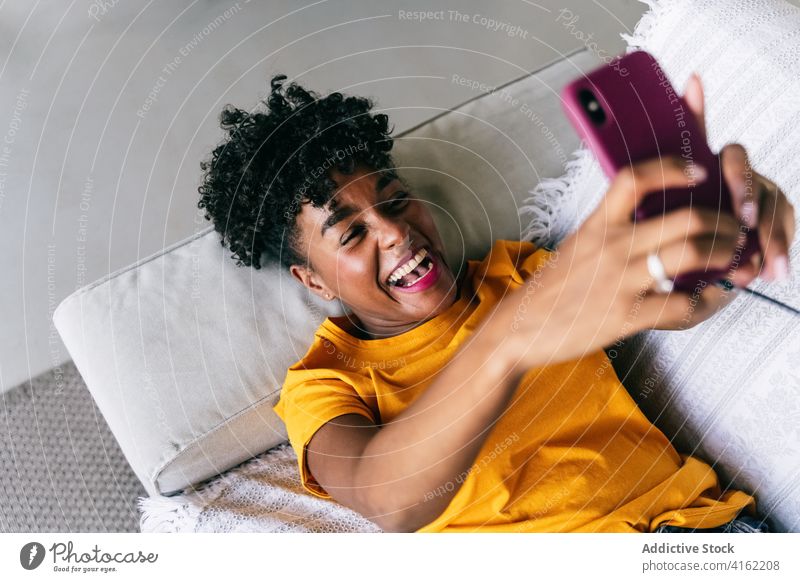 Laughing black woman taking selfie with smartphone at home using laugh having fun excited browsing mobile cheerful millennial young adolescent female modern