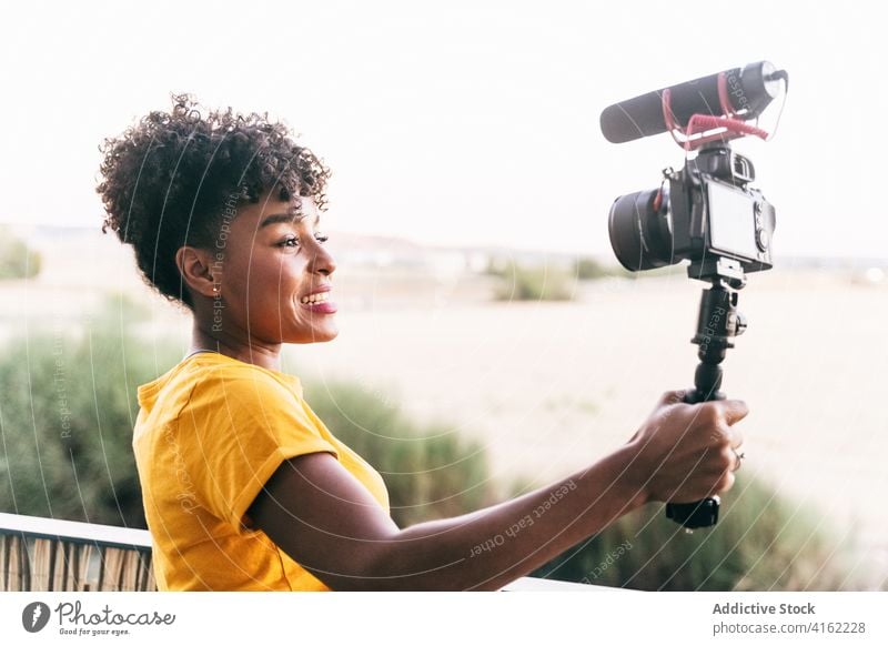 Positive female blogger shooting video on terrace vlog selfie stick camera record cheerful travel happy young woman african american black ethnic excited share