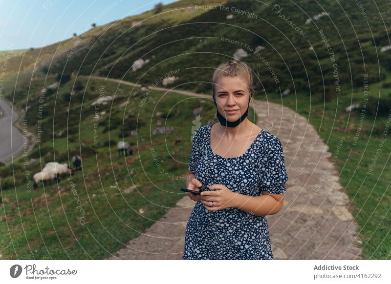 Woman with lowered face mask standing on lush hilly terrain woman positive serene hillside countryside nature charming content amazing mountain environment