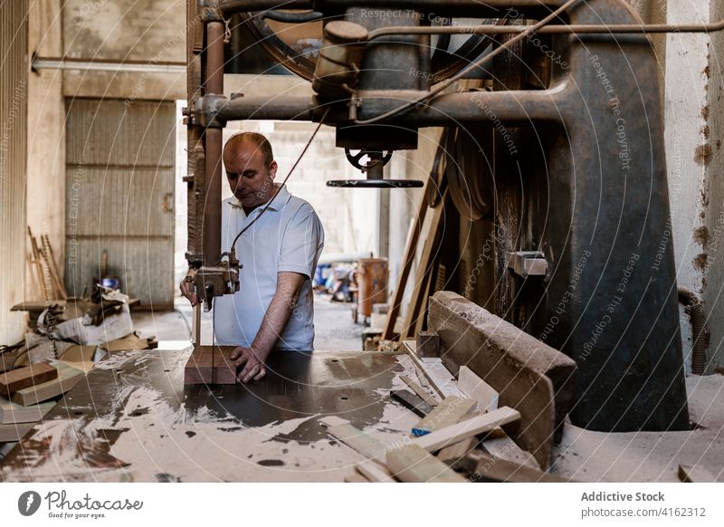 Woodworker cutting lumber plank in workshop band saw wood woodwork man carpenter carpentry woodworker woodcut male wooden workbench messy job craftsman manual