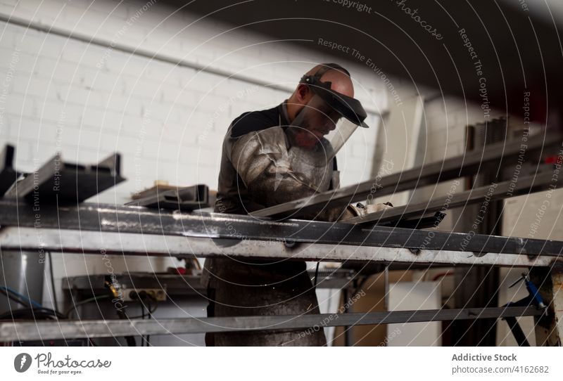 Focused welder in apron in workshop man dirty grunge detail metalwork worker male serious industry tool equipment workbench busy manufacture skill uniform job