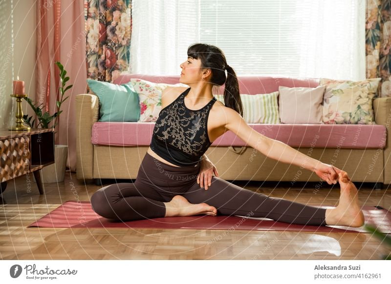 Young beautiful woman practicing yoga at home. Stylish cozy home interior. Doing yoga exercises and enjoying early morning. Healthy lifestyle active activity