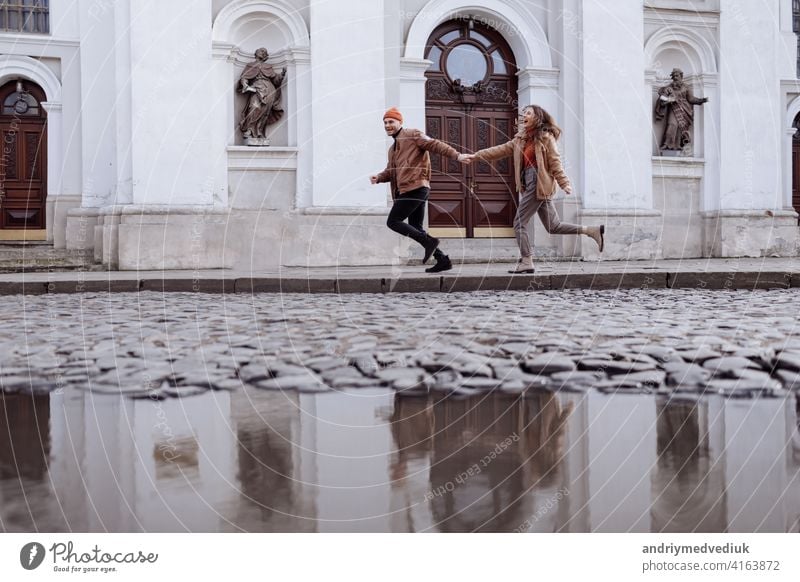 Happy young stylish couple, enjoying their walk in old road in city street with ancient building on the background after rain. selective focus. happy man girl