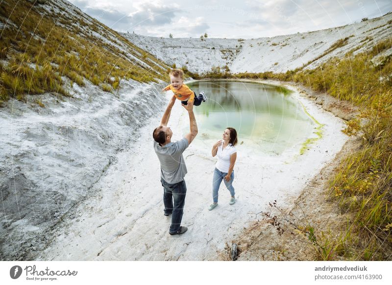 Happy young family near lake, pond. Family enjoying life together at meadow. People having fun in nature. Family bonds outside. Mother, father, child smiling while spending free time outdoors