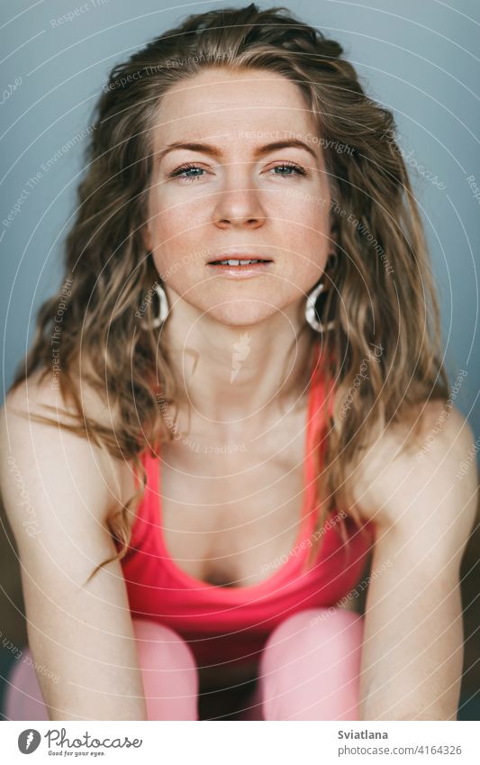 Portrait of a beautiful girl with curly hair in sports clothes on a gray background yoga sportswear portrait indoor practicing studio smiling leisure lifestyle