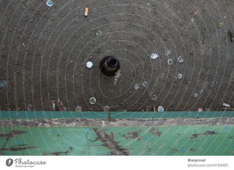 Empty beer bottle, crown corks and cigarette butts in front of a bench in a green area Bench Bottle Park bench Bottle of beer Crown cap tip Drinking Smoking out