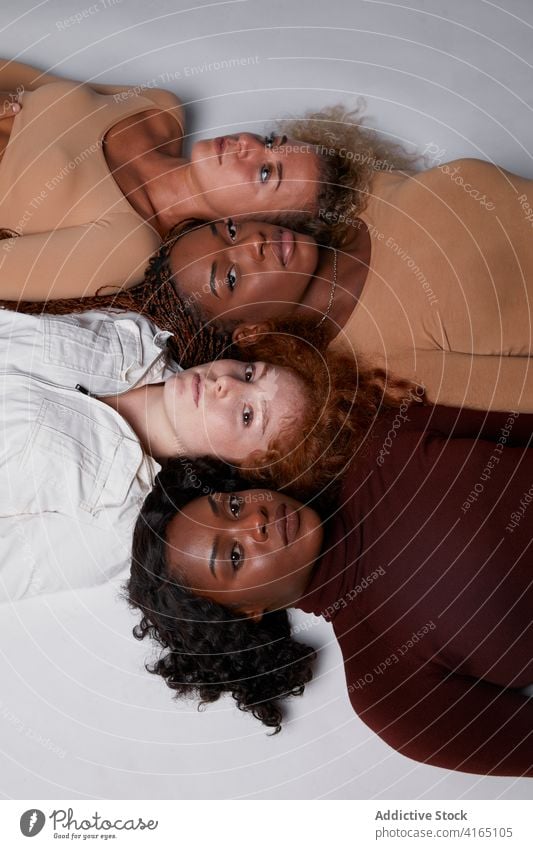 Multiracial women lying in row in studio together model pastel color outfit curly hair multiethnic multiracial diverse black african american line floor rest