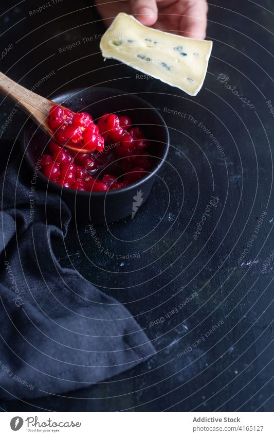 Crop person holding slice of Gorgonzola cheese near mashed currants gorgonzola eat enjoy ripe gourmet tasty berry blend fresh cook process prepare appetizing