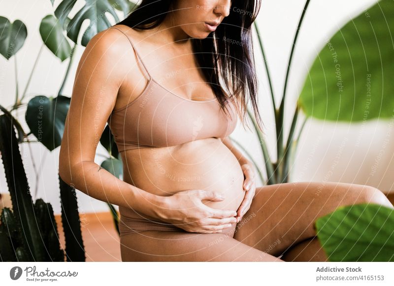 Delicate pregnant woman touching belly in room underwear lingerie prenatal pregnancy delicate tender female stool green tummy expect stomach mother anticipate