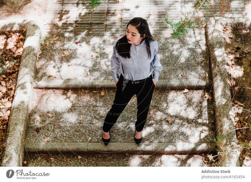 Elegant young ethnic lady resting in autumn park woman style stair elegant hand in pocket well dressed relax pensive fashion nature female asian chinese