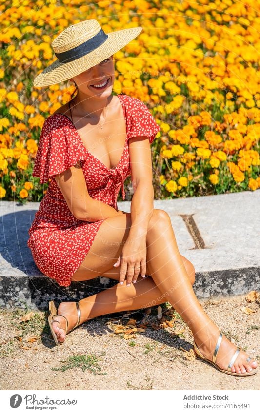 Smiling woman in hat relaxing in botanic garden summer carefree dress smile flower bloom female blossom flowerbed rest chill sit straw hat sunny stone border