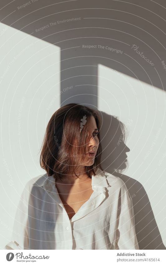 Pensive young woman leaning on white wall on sunny day sensual pensive dreamy feminine sunlight style elegant calm gorgeous tender female brown hair white shirt