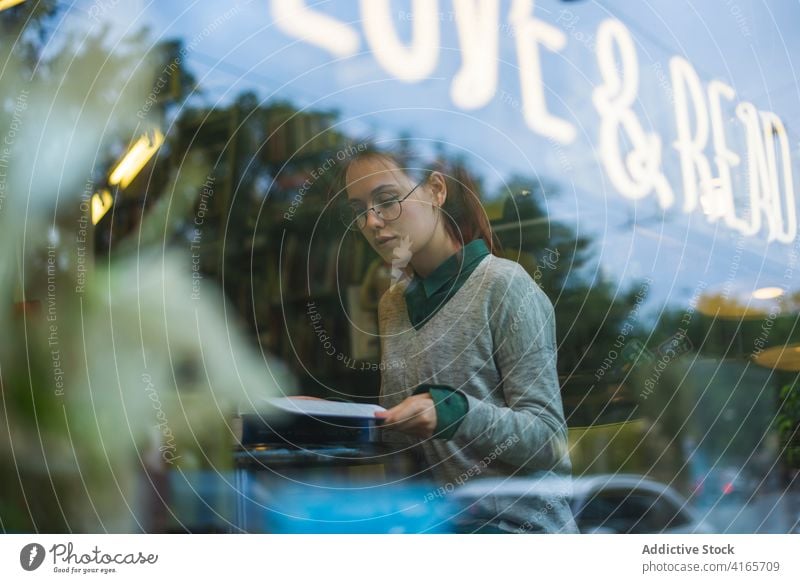 Tranquil woman with book in cozy cafe thoughtful weekend relax smart enjoy style female warm cup literature window table casual beverage through rest think