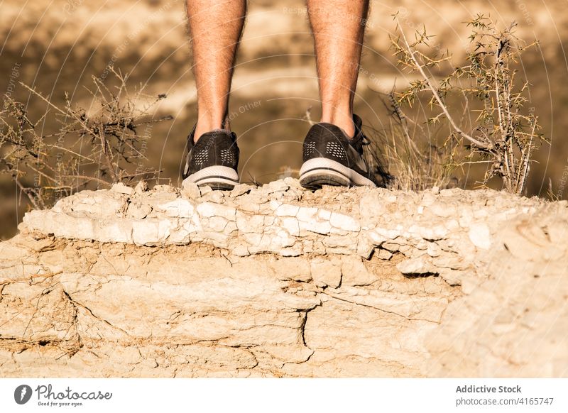 Unrecognizable man running in semi desert area on sunny day jump nature workout training energy sand active terrain runner male sportswear wellness healthy