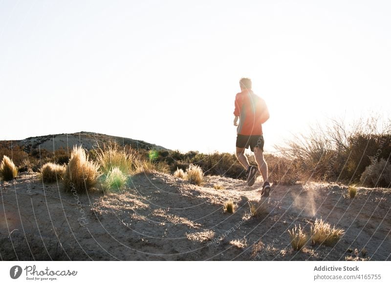 Anonymous sportsman jogging on sandy terrain in mountainous terrain run semi desert hill training active jogger healthy nature wellbeing exercise workout male