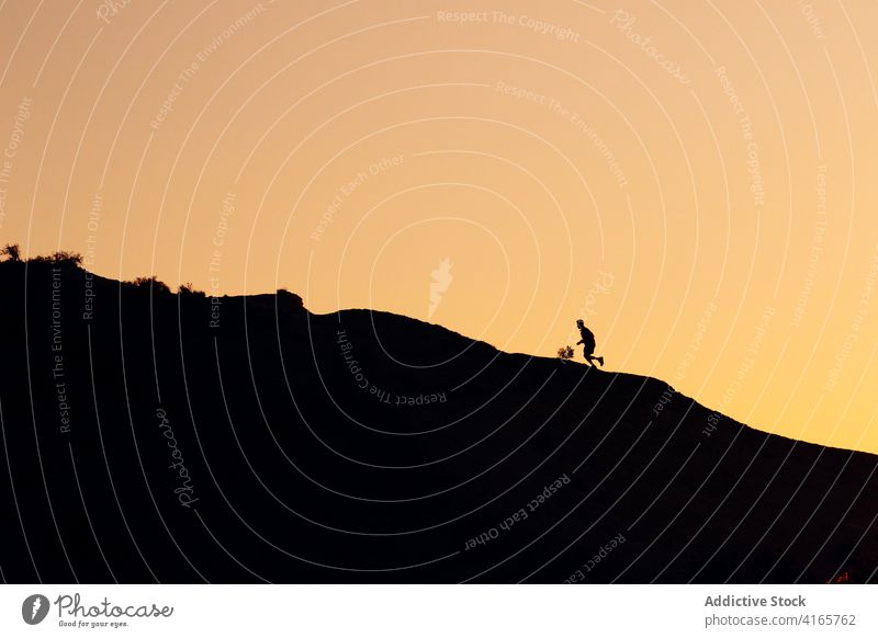 Anonymous person running on hill at sundown mountain slope workout sunset athlete climb training silhouette exercise healthy sport endurance wellness fit nature