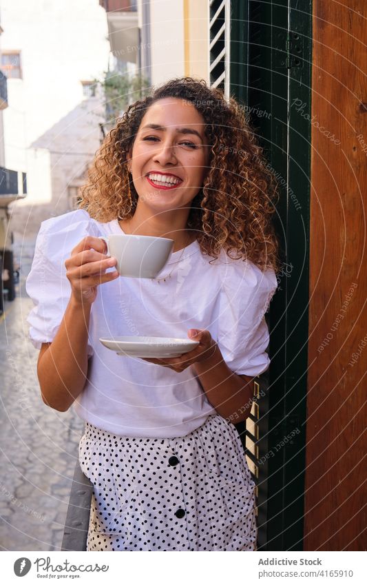 Happy woman enjoying hot drink on balcony rest laugh style hotel weekend break happy female relax cheerful delight cup beverage curly hair smile tea coffee