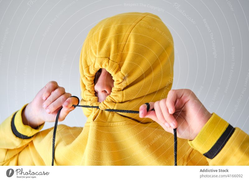 Unrecognizable teen hiding in hood in studio cover hide having fun yellow hoodie teenage style expressive playful childish carefree funny individuality cool