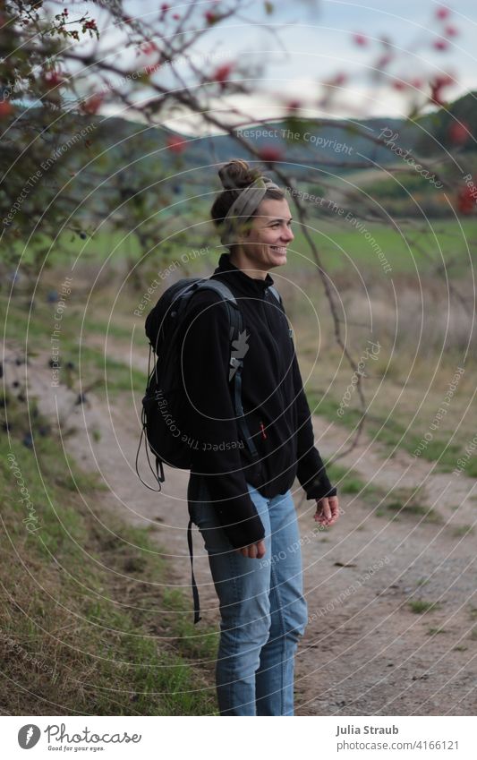 Young woman with hiking backpack on a dirt road under rosehip bush Hiking Autumn Autumnal Rose hip rose-hip bush off the beaten track Field Edge of the forest