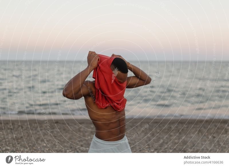 Smiling black man putting on t shirt on beach smile happy put on rest glad athlete coast carefree seashore male runner lifestyle relax water positive