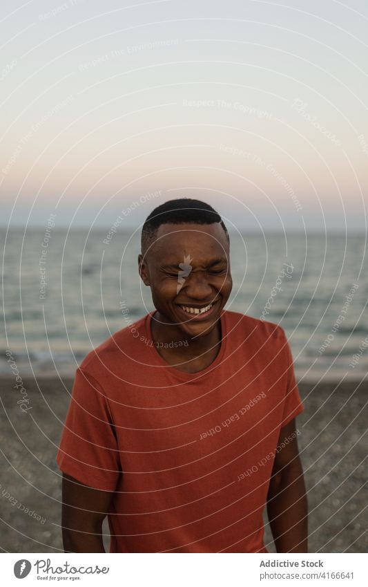 Cheerful black sportsman standing on beach african smiling closed eyes fit strong male sporty serious guy muscle shore confident torso african american seashore