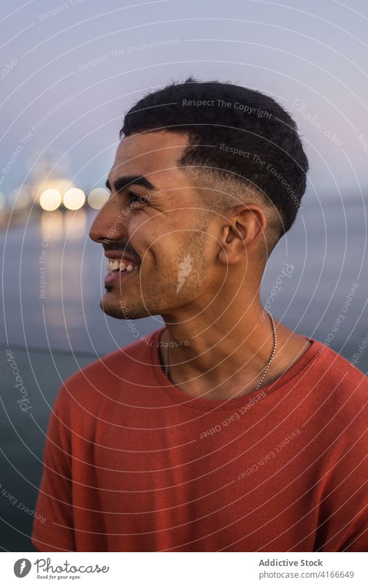 Cheerful ethnic tourist near ocean smile enjoy vacation seascape sky summer twilight man traveler happy sunset water evening scenic idyllic horizon building