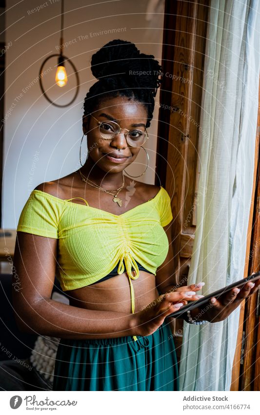 Positive young African American female using tablet at home woman browsing remote job busy positive smile gadget style online internet ethnic african american