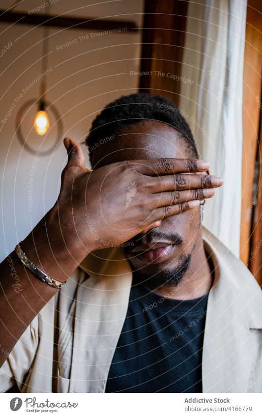 Black man covering face with hand cover eyes palm mystery peaceful home bracelet lamp serious male calm african american black trendy light apartment handsome