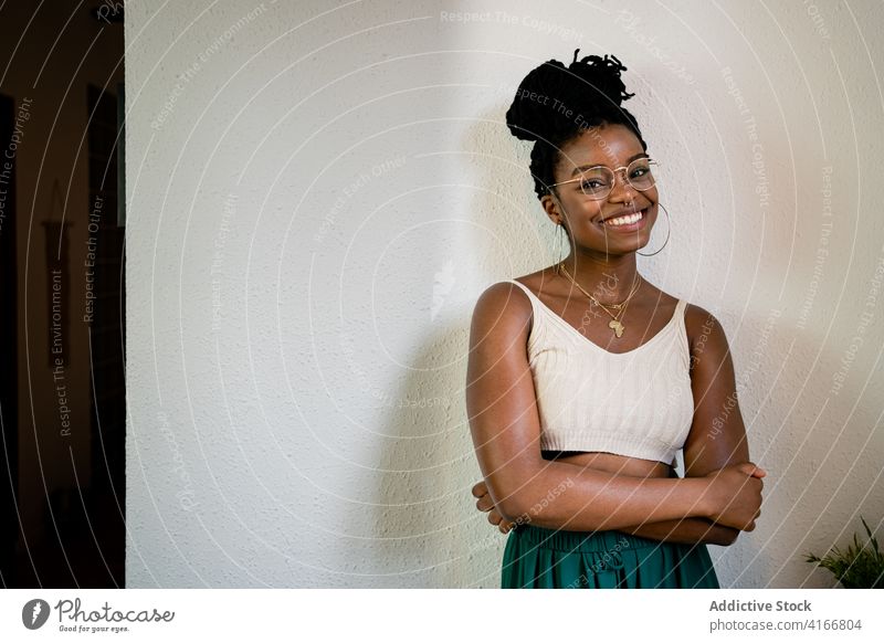 Happy black woman in eyeglasses in room toothy smile hairstyle accessory fashion outfit content cheerful female african american happy brunette joy positive