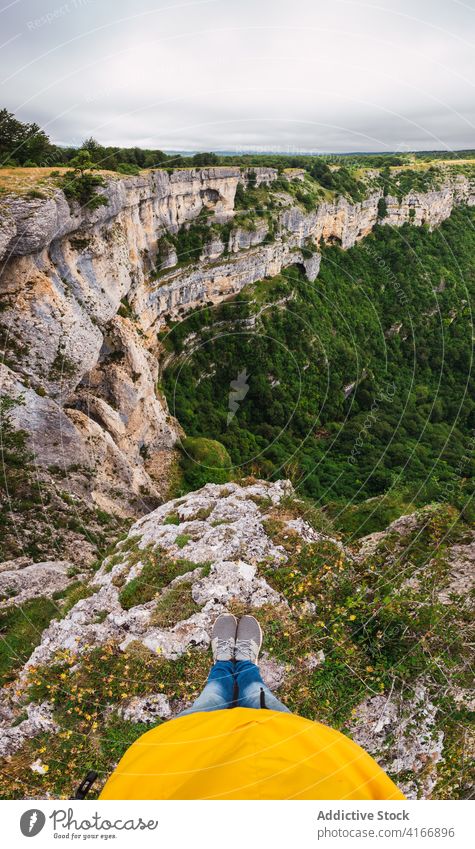 Crop tourist contemplating mountains with greenery trees traveler admire nature highland sky cloudy vegetate atmosphere lying sneakers jeans contemplate rough