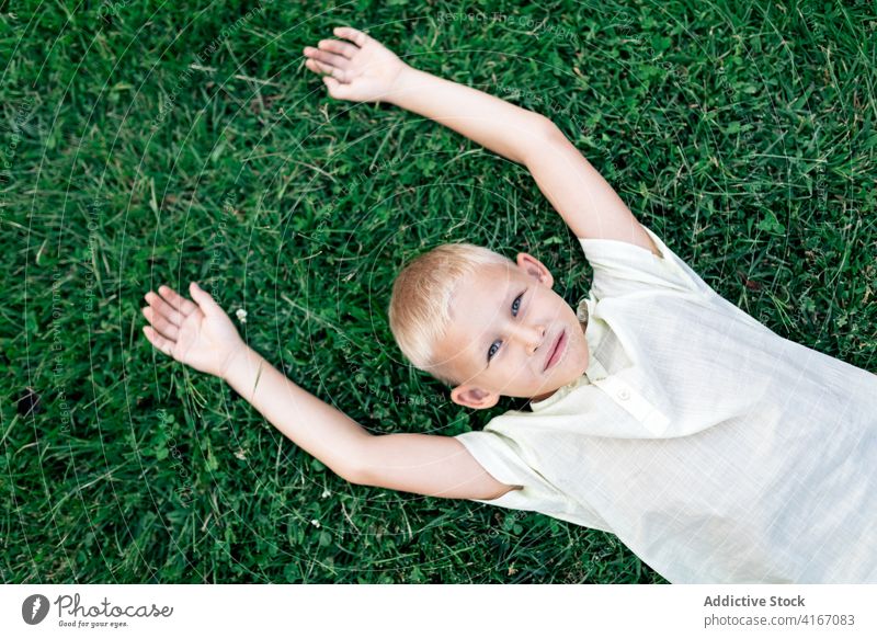 Happy boy resting on lawn in daylight kid happy child grass chill weekend pleasure hand behind head relax cheerful blond childhood carefree summer delight