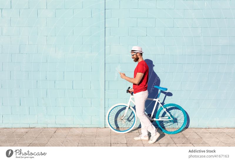 Trendy young man using smartphone near bicycle on street building city street style trendy vehicle sunlight mobile male casual outfit online browsing internet