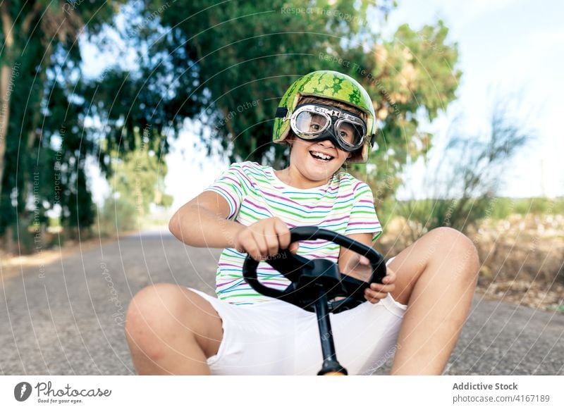 Excited boy riding pedal car on road ride amazed recreation having fun activity excited goggles childhood trendy wear kid go kart transport roadway asphalt