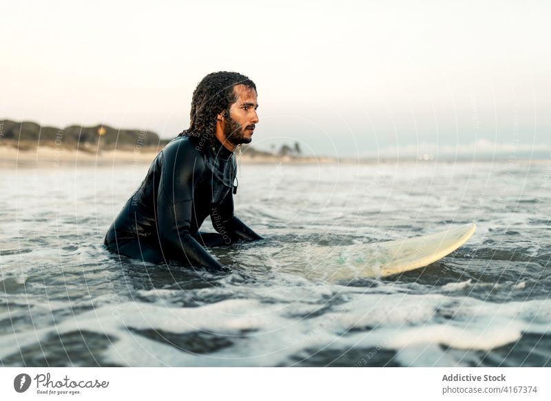 Concentrated surfer looking at coming wave man sea ocean water sports summer focus leisure surfboard male serious pensive curly hair wetsuit vacation beach