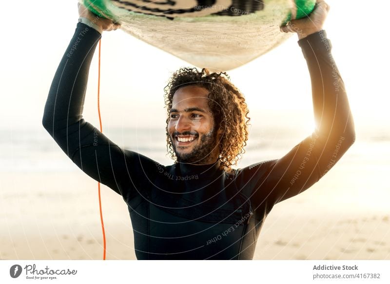 Cheerful surfer holding skimboard over head man cheerful sunset seashore freedom tropical water sports male resort ethnic ocean beach summer swimsuit guy